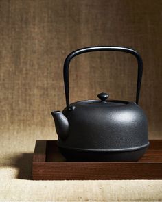 a black tea pot sitting on top of a wooden stand