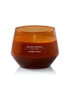 an orange glass candle sitting on top of a white surface with the words spiced pumpkin in