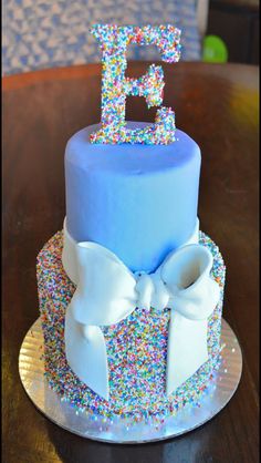 a blue cake with sprinkles and the letter e on top is sitting on a table