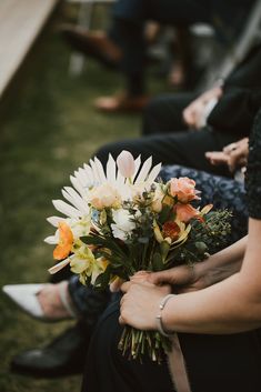 a bouquet of flowers is being held by two women in black dresses and white shoes