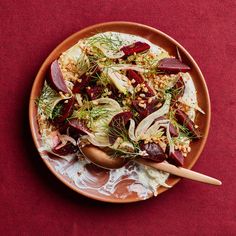 a salad with beets, fennels and nuts on a brown plate next to a wooden spoon