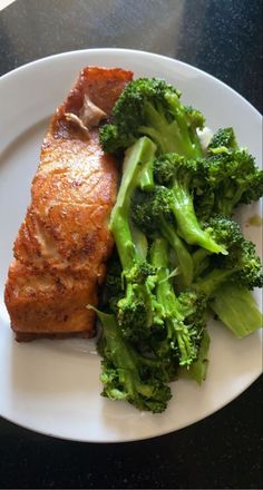 a white plate topped with meat and broccoli on top of a black table