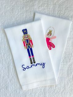 two white towels with embroidered images of nutcrackers and fairy tale characters on them