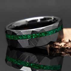 two rings with green and black inlays sitting on top of a piece of wood