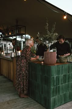 two people standing at a counter in front of a potted plant and another person behind the counter