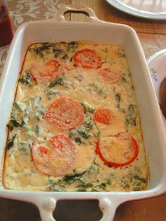 a casserole dish with tomatoes and spinach in it sitting on a table