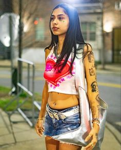 a woman with tattoos is walking down the street in shorts and a cropped top