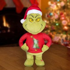 the grinch stuffed toy is wearing a santa hat and has his hands on his hips