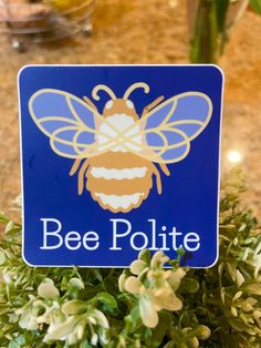 a blue bee pollite sign sitting on top of a planter filled with flowers