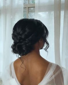 the back of a woman's head in front of a window with sheer curtains