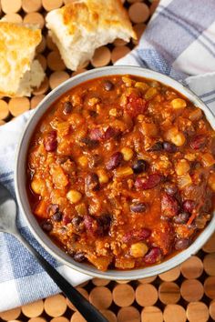 a bowl filled with chili and beans on top of a table next to some bread