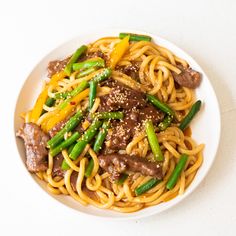 a white plate topped with noodles and meat next to green beans on top of a table