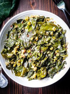 a white bowl filled with collard greens on top of a wooden table next to silverware