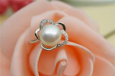 a white pearl and diamond ring sitting on top of a pink rose with diamonds around it