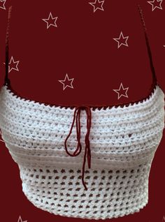 a white crocheted bag with red string and stars on it, sitting against a red background