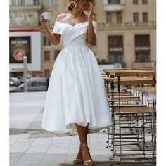 a woman in a white dress is talking on her cell phone and holding a cup