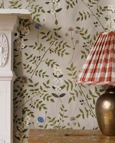 a lamp on a table in front of a wall paper with flowers and leaves pattern