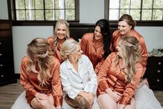 a group of women sitting on top of a bed in matching orange pajamas and ties