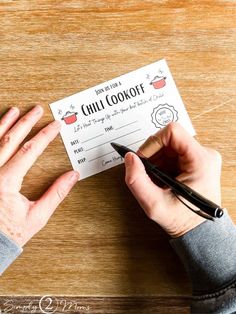 a person holding a pen and writing on a paper with the words chili cook off