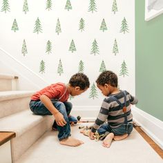 two young boys playing with toys on the floor in front of a christmas tree wall decal