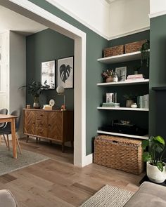 a living room with green walls and white trim on the wall, wicker baskets in front of the bookshelf