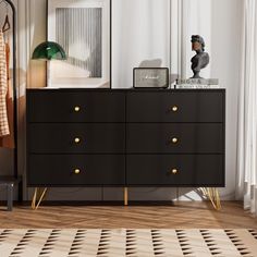 a black dresser with gold handles and knobs in a white room next to a window