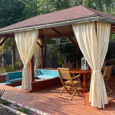 a gazebo with curtains on the sides and a pool in the middle next to it