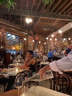 people sitting at tables in a restaurant with lights hanging from the ceiling and wood floors