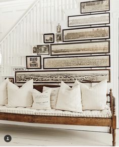 a bench with many pillows on it in front of a stair case filled with pictures