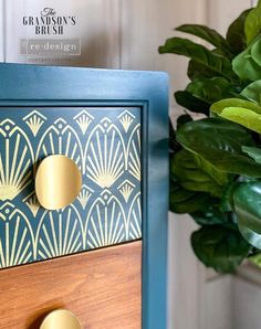 a close up of a blue dresser with gold knobs on it and a potted plant in the background