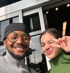 a man and woman posing for the camera with their fingers in the shape of a heart