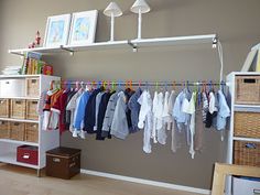 an organized closet with clothes hanging from the ceiling and baskets on the floor next to it