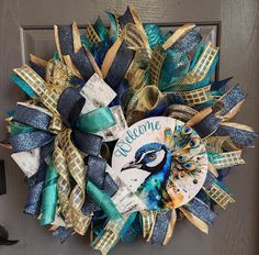 a peacock welcome wreath is hanging on the front door with blue, gold and green ribbons