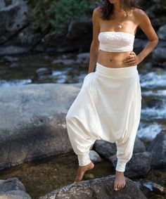 a woman standing on top of a rock next to a river wearing a white skirt