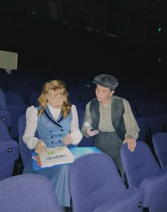 a man and woman sitting on blue chairs in front of a table with a book