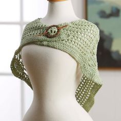 a white mannequin wearing a green crochet shawl with a button