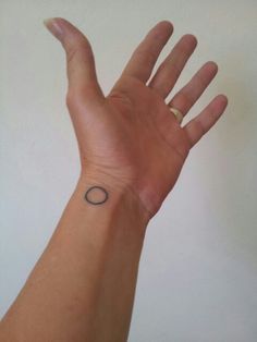 a person's hand with a small black circle tattoo on the middle of it