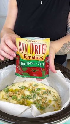 a woman holding a bag of sun dried tomatoes in front of a crock pot