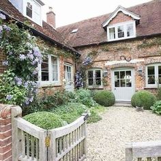 an old brick house with flowers growing on the front and side walls, along with a wooden gate