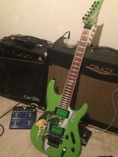 a green guitar sitting on the floor next to two amps