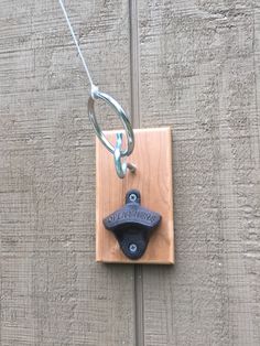 a piece of wood with a metal hook attached to it on a chain that is hanging from the side of a wall