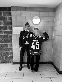 a man and woman standing next to each other in front of a brick wall with the number 46 on it