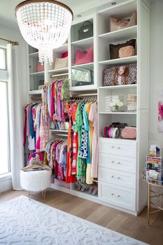 a white closet filled with lots of clothes and other items next to a chandelier