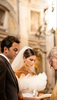 the bride and groom are looking down at their vows in front of an older man