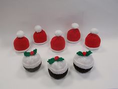 six knitted cupcakes with hats and bows are arranged in the shape of santa's hat