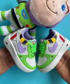 a hand holding two stuffed toys in front of a blue background with a green and white nike air force shoe