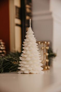 a small white christmas tree sitting on top of a table next to a gold candle