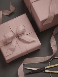 a pair of scissors sitting next to a pink gift wrapped in satin ribbon and bow