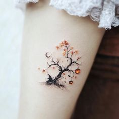 a woman's leg with a tree and pumpkins tattooed on the side of her thigh