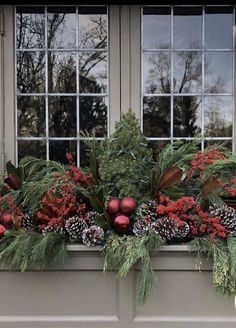 a window box filled with christmas decorations and greenery next to two windowsills